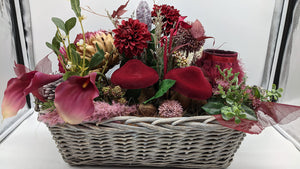 Herbstgesteck im grauen Weidenkorb mit roten Pilzen, bordeauxfarbenen Dahlien, pinken Calla und rotem Teelichtglas