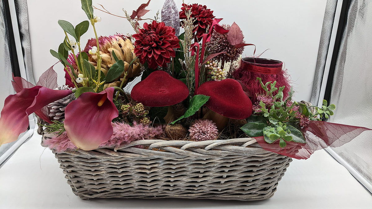 Tischgesteck in Bordeaux und Rosa mit Artischocke, Misteln, Beeren und Zapfen im Korb, seitliche Ansicht