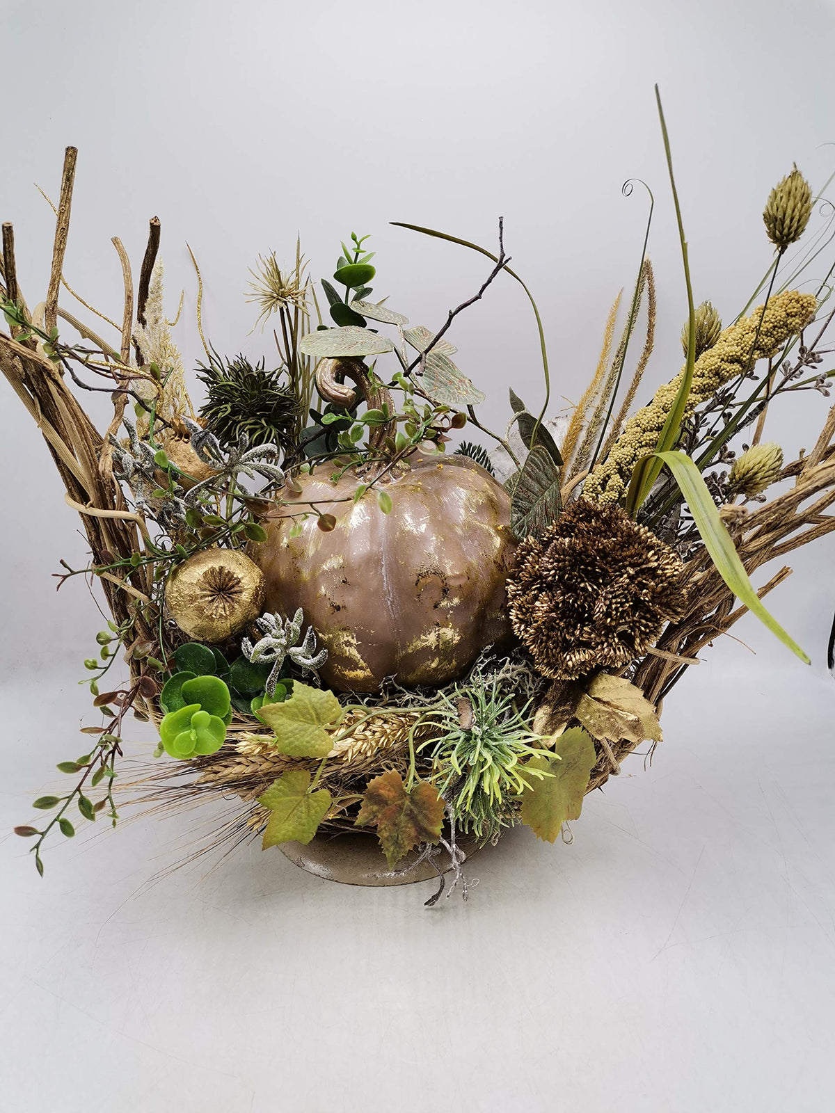 Herbstgesteck seitlich: Kürbis in Altrosa-Gold, Sedumdolde, Weinlaub und Hirse auf flacher Metallschale