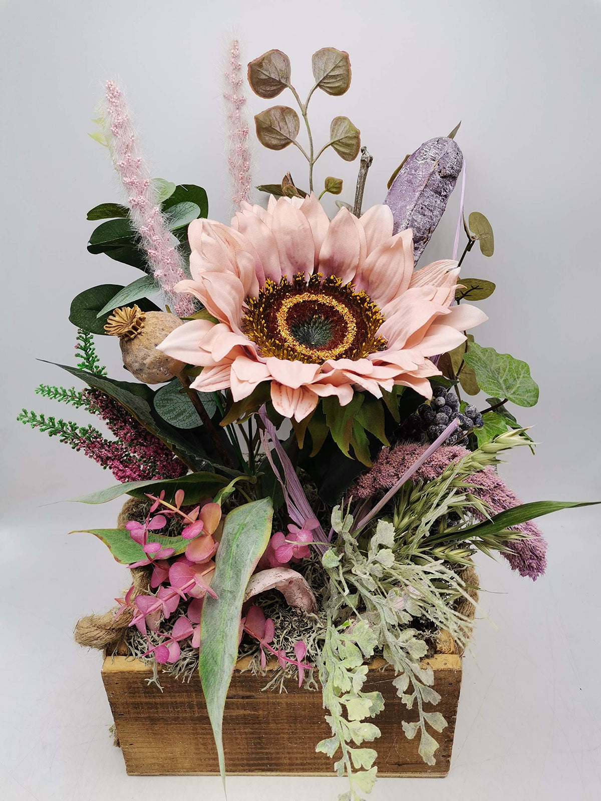 Herbstgesteck von vorn: rosa Sonnenblume mit brauner Mitte, Beeren, Farn und lila Rispen im Holzkasten
