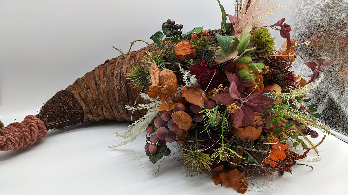 Längliches Füllhorn aus Rinde mit Herbstgesteck aus Kürbis, Trauben, Laub und Gräsern in Orange und Braun