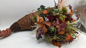Längliches Füllhorn aus Rinde mit Herbstgesteck aus Kürbis, Trauben, Laub und Gräsern in Orange und Braun
