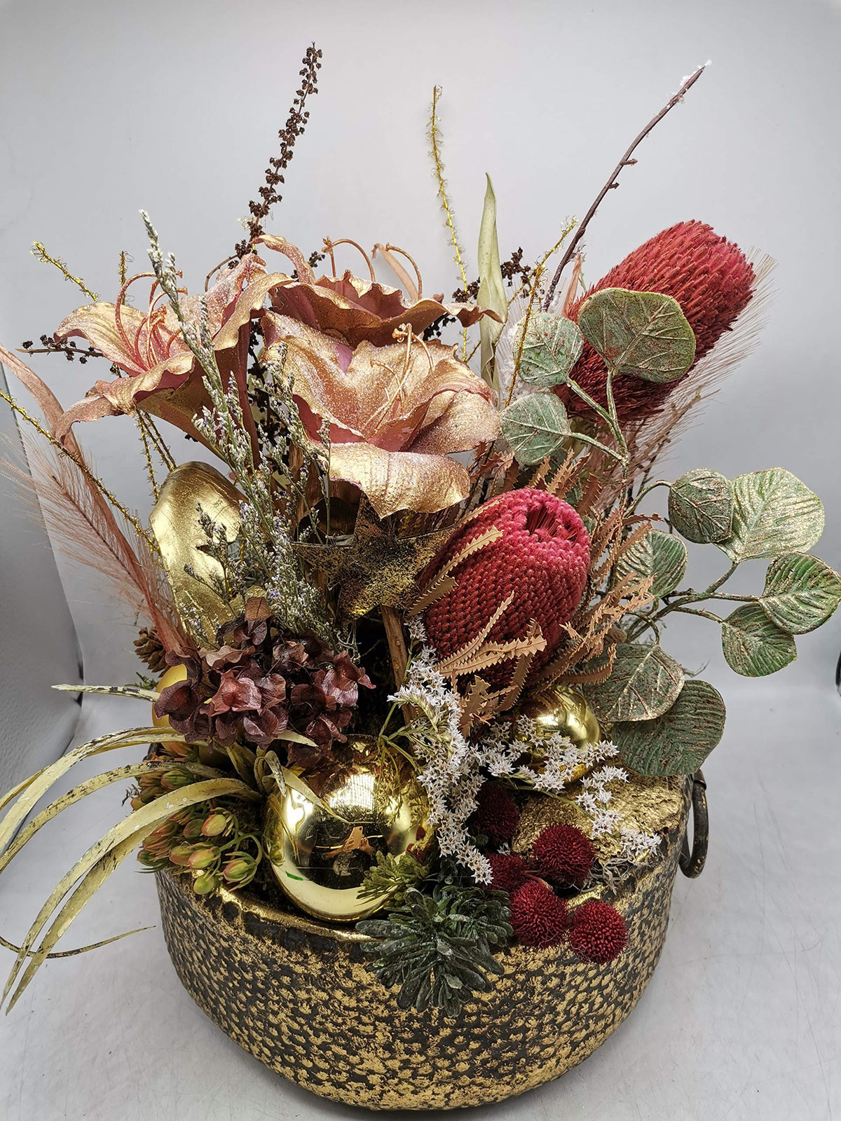 Herbstgesteck von vorn: rote Banksia, Hortensien, Eukalyptuslaub und goldene Kugeln in runder Metallschale