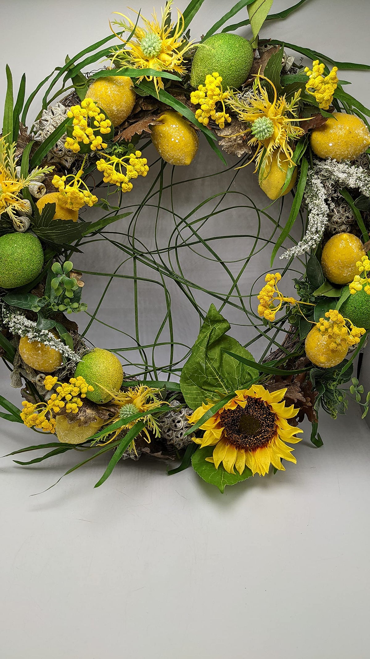 Sommerkranz mit Sonnenblume, gelben Zitronen, grünen Limonen und Gräsern auf hellem Untergrund
