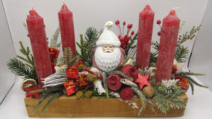 Adventsgesteck im Holzkasten mit vier roten Kerzen, Weihnachtsmann, roten Geschenken, Mohnkapseln und Tannenzweigen