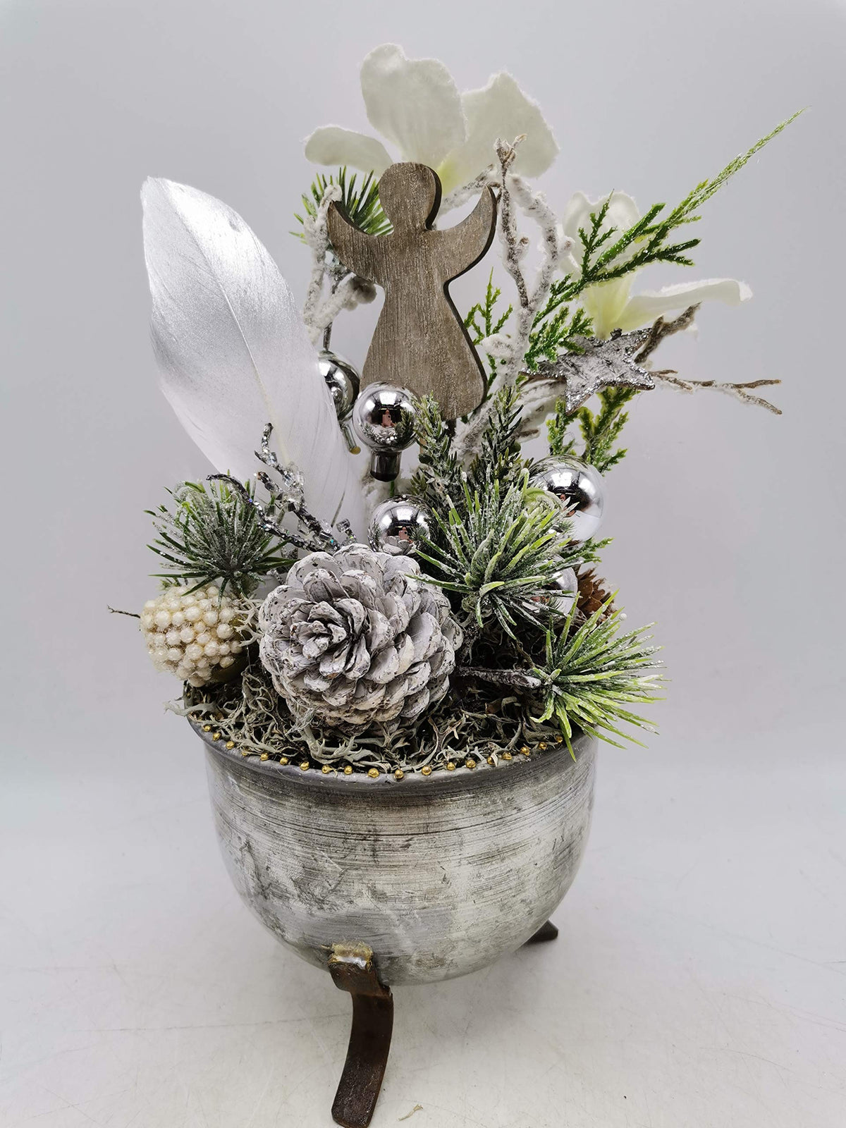 Weihnachtsgesteck in silbergrauer Schale auf Füßen mit Holzengel, weißen Blüten, Silberkugeln und Zapfen